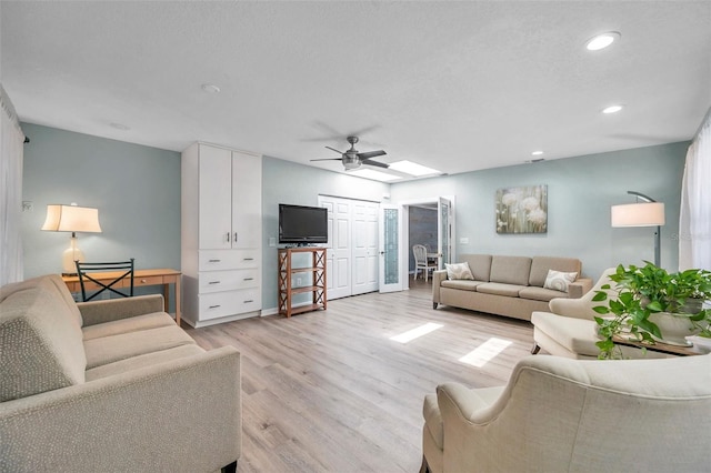 living room with ceiling fan, light hardwood / wood-style flooring, a textured ceiling, and a skylight