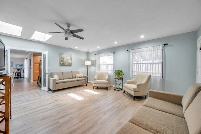 living room with light hardwood / wood-style floors, ceiling fan, and a skylight