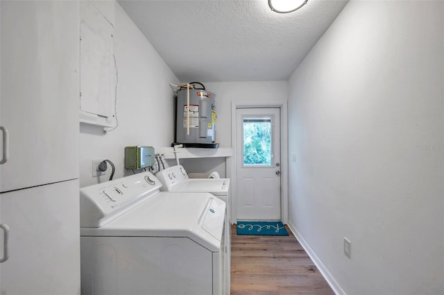 washroom with a textured ceiling, water heater, washing machine and clothes dryer, and light wood-type flooring