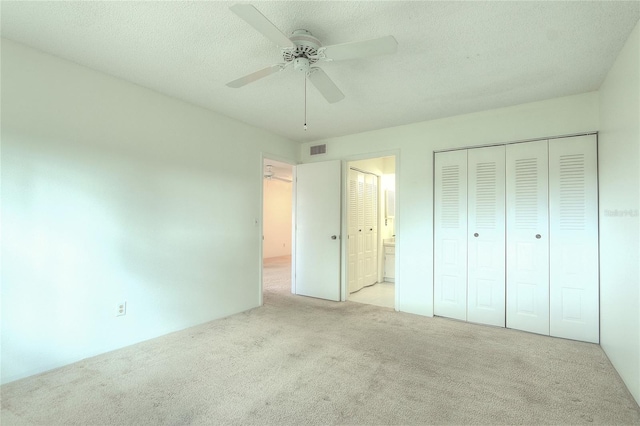 unfurnished bedroom featuring ensuite bath, light carpet, a textured ceiling, a closet, and ceiling fan