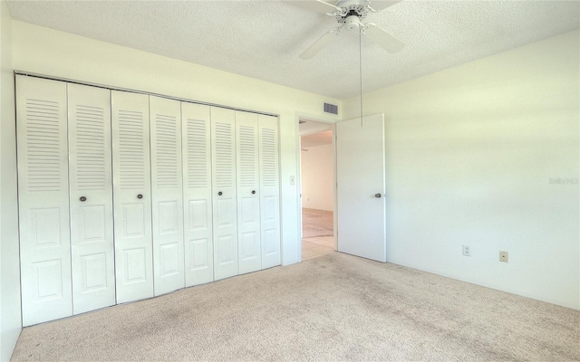 unfurnished bedroom featuring ceiling fan, light colored carpet, a textured ceiling, and a closet