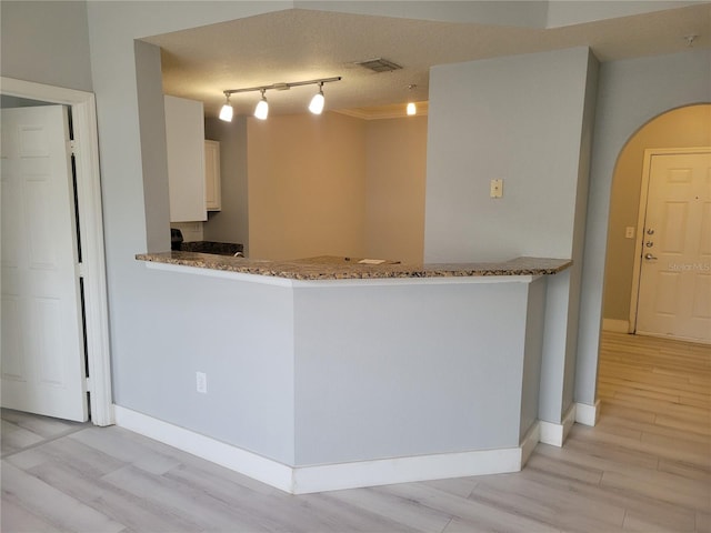 kitchen with stone counters, white cabinetry, light hardwood / wood-style floors, a textured ceiling, and kitchen peninsula