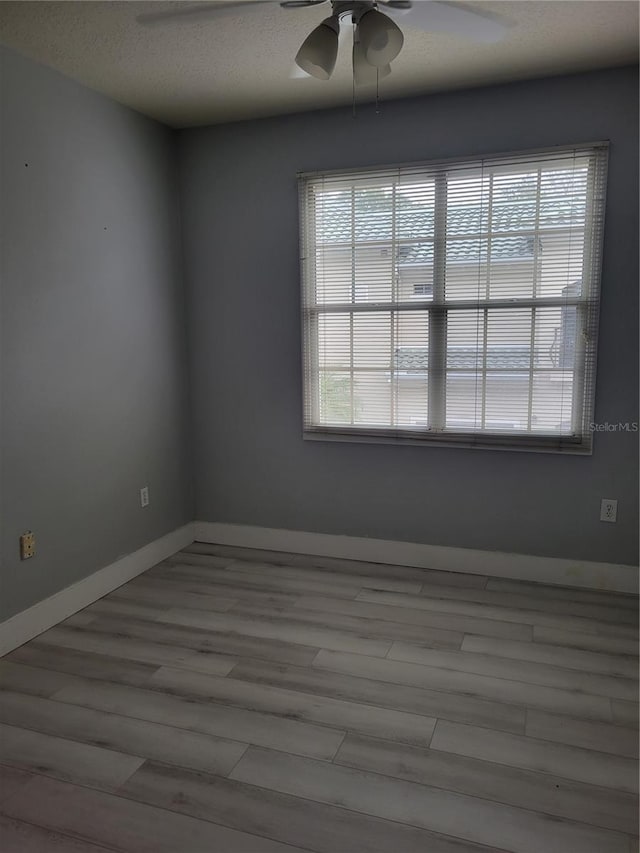 empty room with a textured ceiling, a wealth of natural light, ceiling fan, and light wood-type flooring