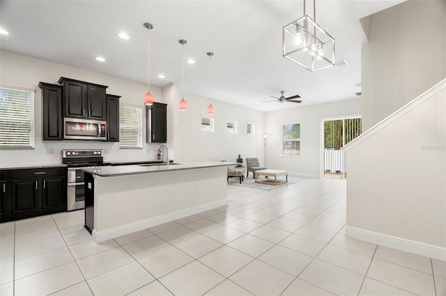 kitchen with appliances with stainless steel finishes, a kitchen island with sink, pendant lighting, and light tile patterned floors