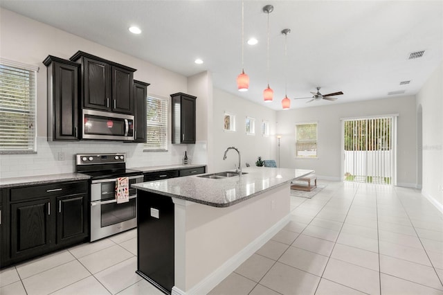 kitchen featuring sink, tasteful backsplash, appliances with stainless steel finishes, pendant lighting, and a kitchen island with sink