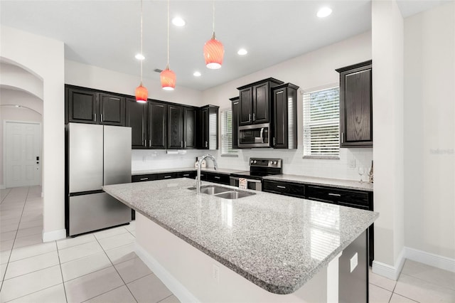 kitchen with stainless steel appliances, decorative light fixtures, sink, and a center island with sink