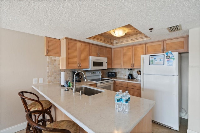 kitchen featuring a tray ceiling, backsplash, white appliances, and kitchen peninsula