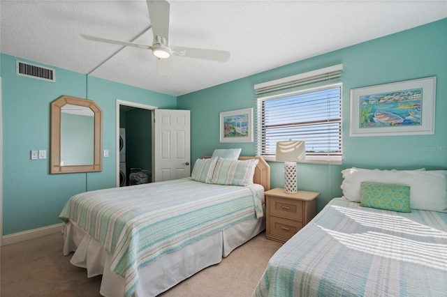 bedroom with light carpet, a textured ceiling, ceiling fan, and stacked washer / dryer