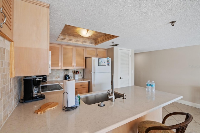 kitchen with light brown cabinetry, sink, a textured ceiling, a raised ceiling, and white fridge