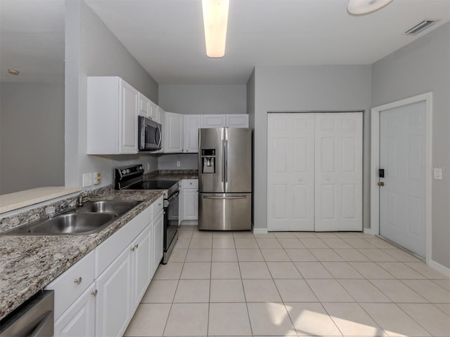 kitchen featuring sink, white cabinetry, light stone counters, light tile patterned floors, and appliances with stainless steel finishes