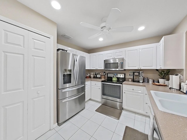 kitchen with sink, light tile patterned floors, ceiling fan, appliances with stainless steel finishes, and white cabinets