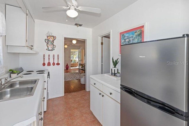 kitchen with sink, white cabinetry, light tile patterned floors, stainless steel refrigerator, and ceiling fan