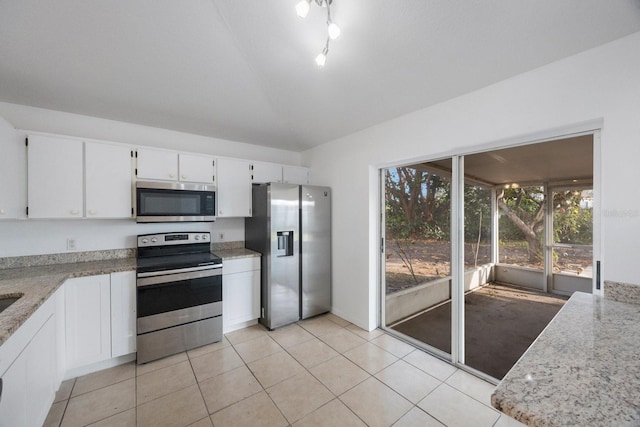 kitchen featuring lofted ceiling, light tile patterned floors, appliances with stainless steel finishes, white cabinetry, and light stone countertops