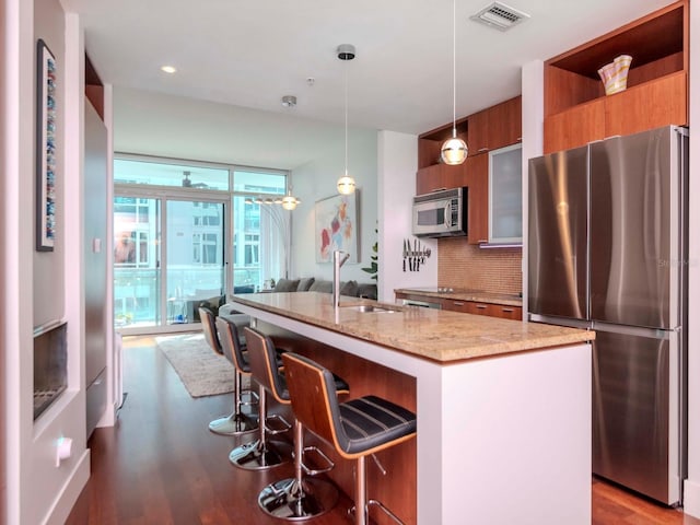 kitchen featuring sink, appliances with stainless steel finishes, a kitchen island with sink, light stone counters, and decorative light fixtures