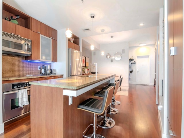 kitchen with a breakfast bar, sink, hanging light fixtures, stainless steel appliances, and a center island with sink