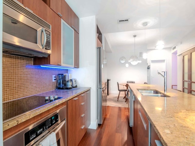 kitchen featuring sink, tasteful backsplash, hanging light fixtures, appliances with stainless steel finishes, and dark hardwood / wood-style floors