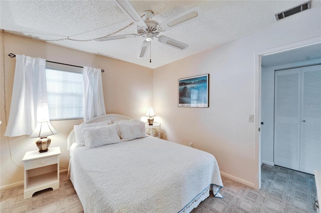 bedroom with ceiling fan, light colored carpet, a textured ceiling, and a closet