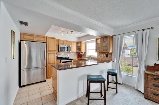 kitchen featuring a textured ceiling, dark stone countertops, appliances with stainless steel finishes, kitchen peninsula, and backsplash