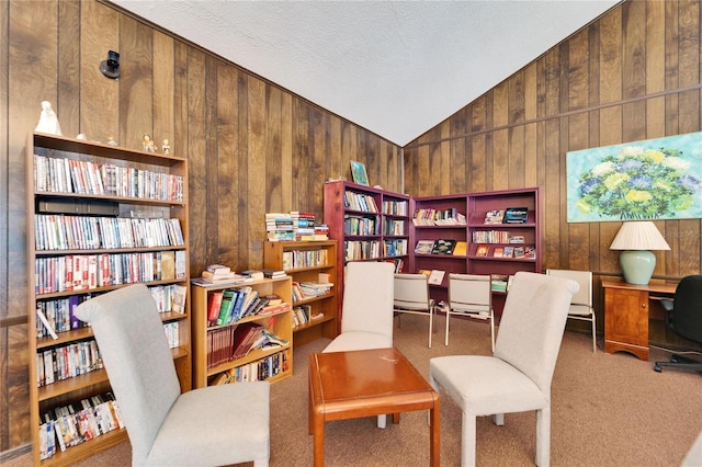 sitting room with lofted ceiling, wooden walls, carpet floors, and a textured ceiling