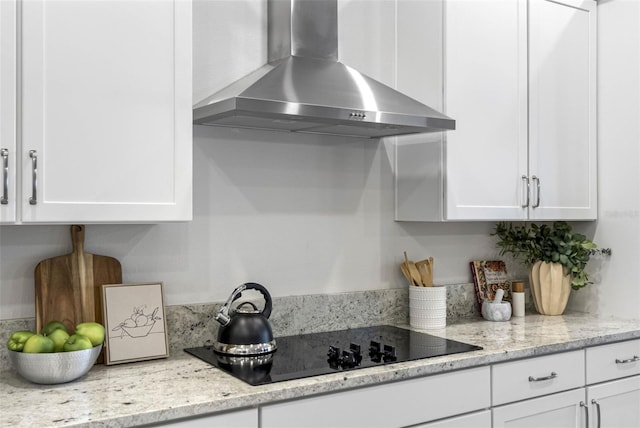 kitchen featuring black electric stovetop, wall chimney exhaust hood, light stone countertops, and white cabinets