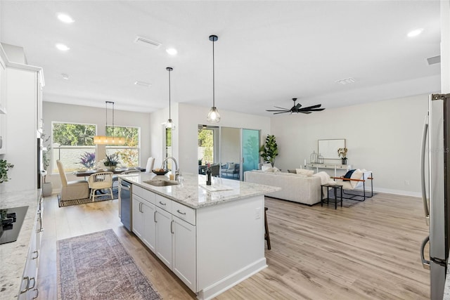 kitchen with sink, a center island with sink, stainless steel appliances, light stone countertops, and white cabinets