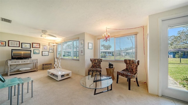 living area with ceiling fan with notable chandelier, plenty of natural light, a textured ceiling, and carpet flooring