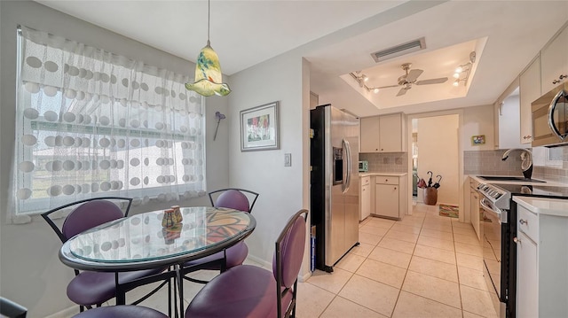 tiled dining area with a raised ceiling and ceiling fan