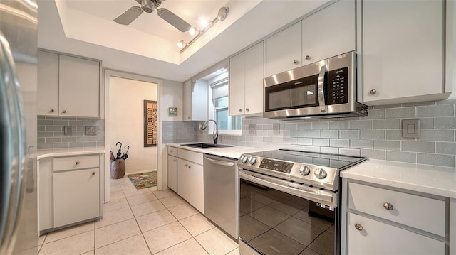 kitchen with sink, appliances with stainless steel finishes, a tray ceiling, ceiling fan, and backsplash