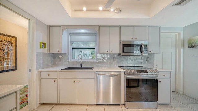 kitchen featuring sink, light tile patterned floors, a raised ceiling, stainless steel appliances, and backsplash