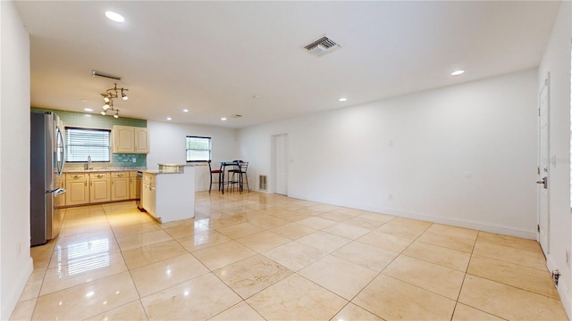 kitchen with light tile patterned flooring, sink, light stone counters, stainless steel refrigerator, and backsplash