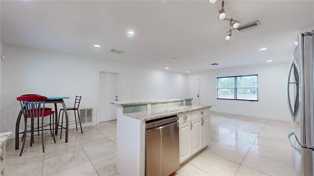 kitchen with light stone counters, light tile patterned floors, appliances with stainless steel finishes, a kitchen island, and white cabinets