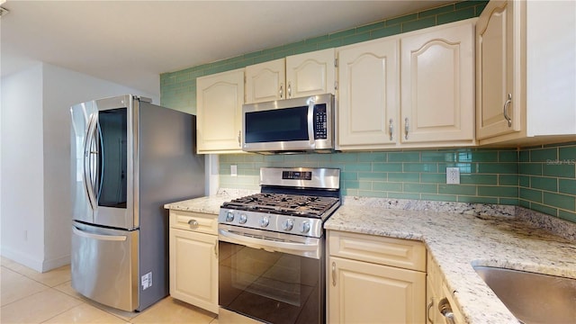 kitchen with stainless steel appliances, light stone countertops, light tile patterned floors, and backsplash