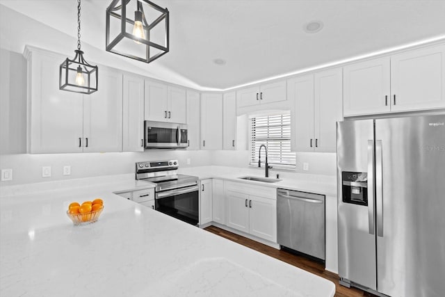 kitchen with sink, appliances with stainless steel finishes, white cabinetry, hanging light fixtures, and light stone counters