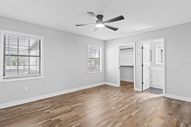 unfurnished bedroom with connected bathroom, a walk in closet, a closet, ceiling fan, and hardwood / wood-style floors