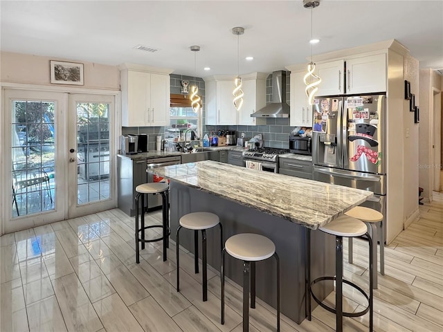 kitchen with stainless steel appliances, pendant lighting, white cabinets, and wall chimney exhaust hood