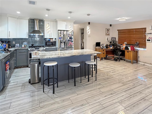 kitchen featuring appliances with stainless steel finishes, a center island, white cabinets, decorative light fixtures, and wall chimney exhaust hood