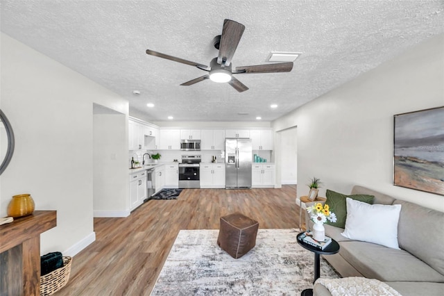 living room with ceiling fan, sink, a textured ceiling, and light hardwood / wood-style floors