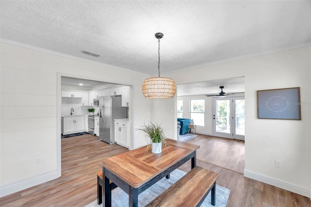 dining area with sink, ornamental molding, light hardwood / wood-style floors, and a textured ceiling