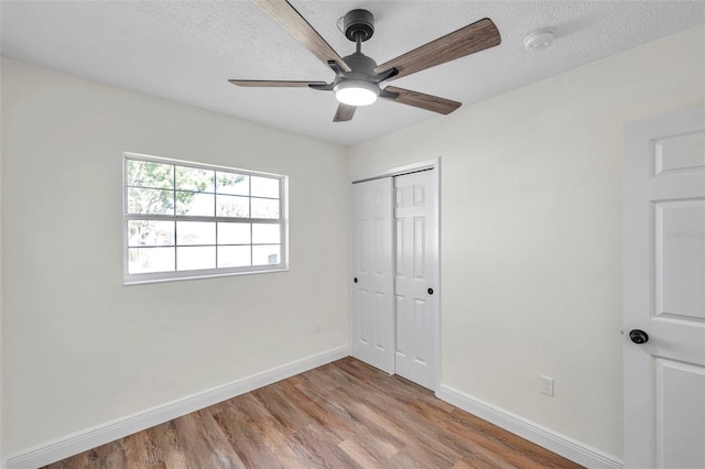 unfurnished bedroom featuring ceiling fan, a textured ceiling, light wood-type flooring, and a closet