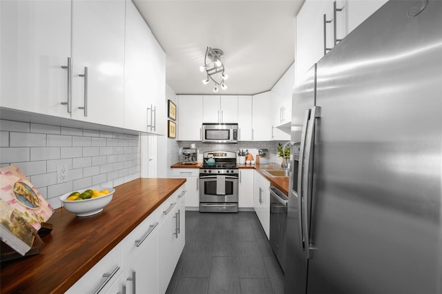 kitchen with appliances with stainless steel finishes, wood counters, sink, backsplash, and white cabinets