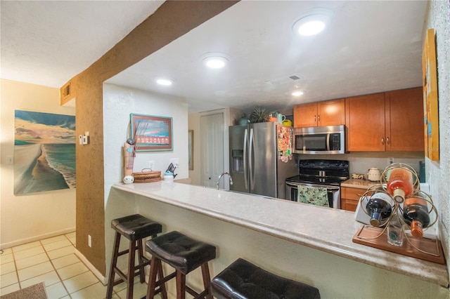 kitchen featuring stainless steel appliances, kitchen peninsula, a breakfast bar area, and light tile patterned floors