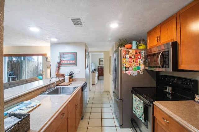 kitchen with appliances with stainless steel finishes, sink, a textured ceiling, and light tile patterned floors