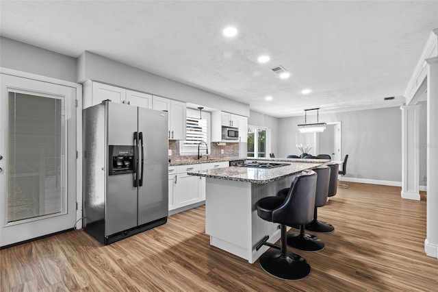 kitchen featuring stone counters, appliances with stainless steel finishes, white cabinetry, hanging light fixtures, and a center island