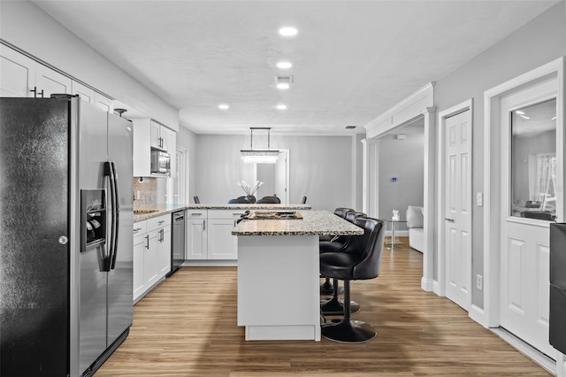 kitchen with a breakfast bar area, light stone counters, a center island, appliances with stainless steel finishes, and white cabinets