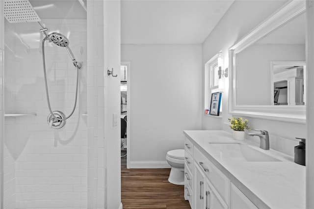 bathroom featuring a tile shower, hardwood / wood-style floors, vanity, and toilet