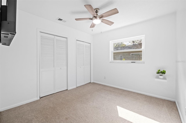 unfurnished bedroom with multiple closets, light carpet, and ceiling fan