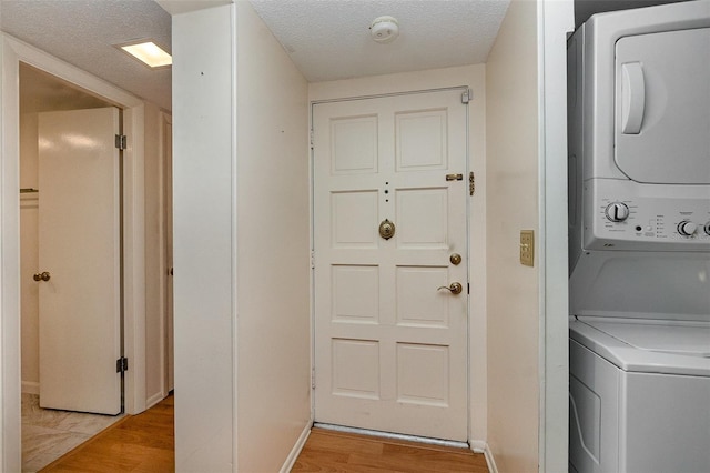 clothes washing area with stacked washer / drying machine, a textured ceiling, and light hardwood / wood-style floors