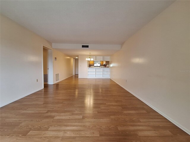 unfurnished living room with wood-type flooring and an inviting chandelier