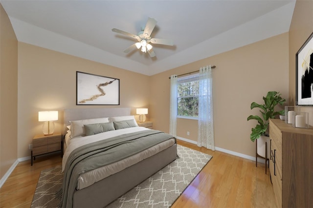 bedroom featuring ceiling fan, a tray ceiling, and light hardwood / wood-style floors