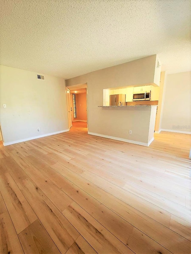 unfurnished living room featuring a textured ceiling, light wood-type flooring, visible vents, and baseboards